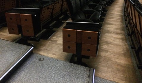 dunkle Stühle (dunkles Holz und schwarze Polster) in leicht geschwungenen Reihen über Holzboden.