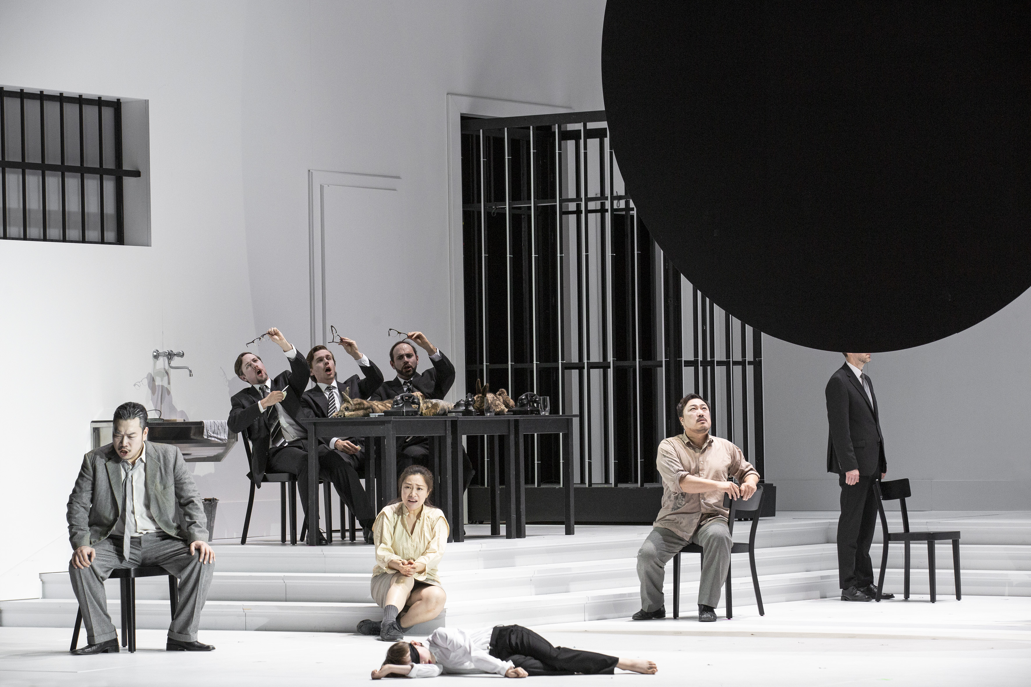 v.l.n.r. Inho Jeong (Timur; sitzend), Guanqun Yu (Li&ugrave;; auf den Stufen sitzend) und Alfred Kim (Calaf; auf dem Stuhl sitzend) sowie Ensemble. Foto: Bernd Uhlig