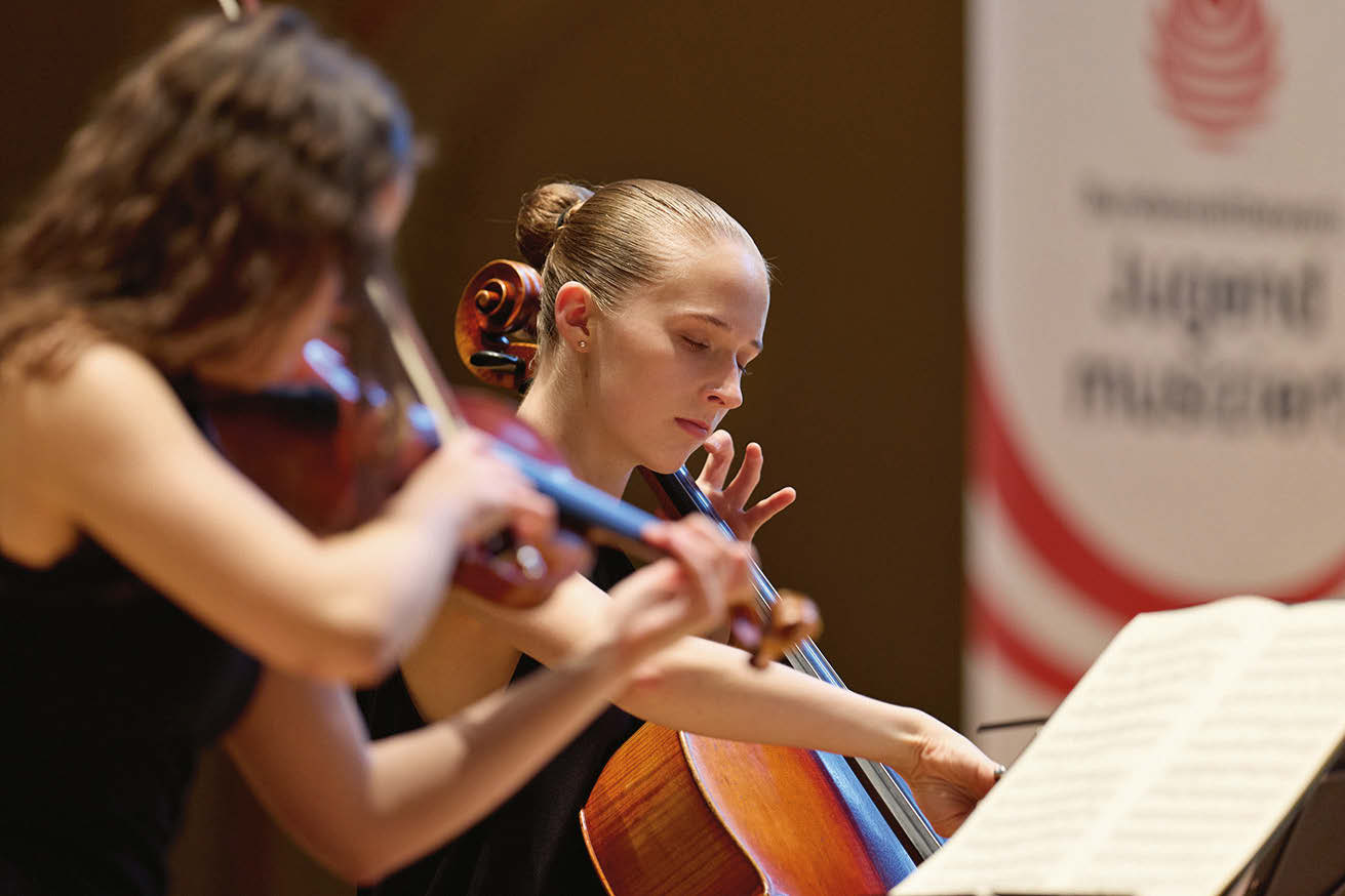 Eine Cellistin mit eng nach hinten zum Dutt gebundenen Haaren und eine Violinistin mit lockigen Haaren