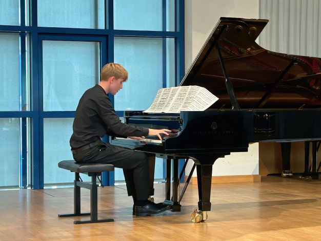 Ein blonder Pianist mit kurzen Haaren und in langer Schwarzer Kleidung spielt von einer langen schlange Notenbl&auml;tter auf dem Fl&uuml;gel.