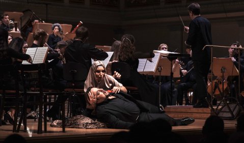 Eine halbszenische Operninszenierung. Vor dem Orchester auf der Bühne, hält Lidia Fridman als Dalinda ihren vergifteten Sohn Ildemaro (Luciano Ganci) liegend im Arm.