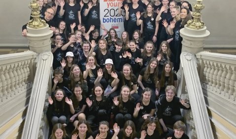 Das Bild zeigt das Orchester des Schyren-Gymnasiums Pfaffenhofen beim Wettbewerb in Prag. Eine Menge schwarz gekleideter Schülerinnen und Schüler sind auf einer Treppe in einem ehrwürdigen Altbau versammelt.