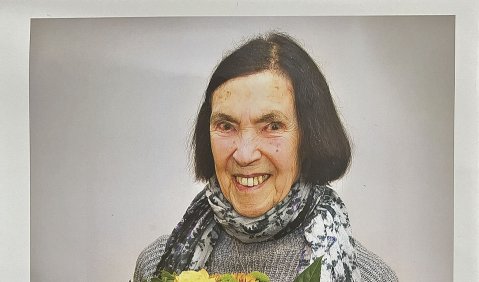Portrait der lächelnden 91-Jährigen mit Blumenstrauß und Schal.