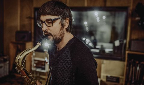 Das Foto zeigt Sandi Kuhn, kurze braune Haare, Brille, sein Saxophon spielend im Studio.