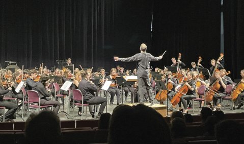 Eine dunkle, aber hell erleuchtete Bühne mit einem Orchester aus zahlreichen jungen Musiker*innen.