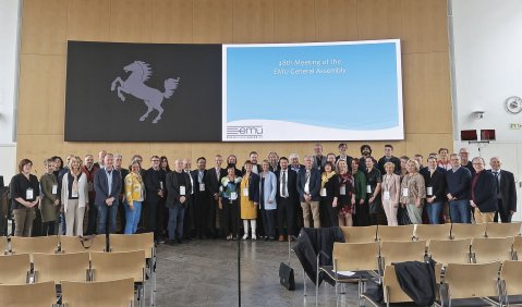 Eine große Gruppe aus Verbandsmitgliedern und geladenen Gästen steht vor einer Wand mit großer Leinwand im Tagungssaal des Stuttgarter Rathauses.