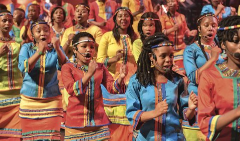 Südafrikanische Jugendliche singen und klatschen in bunter Konzertkleidung.