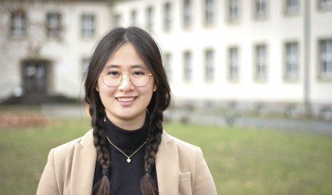 Eine junge Frau in beigem Blazer im Innenhof eines Altbaus