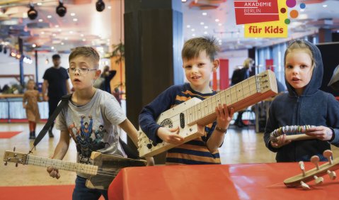 Die 3 Kinder im Grudnschulalter halten selbstgebaute Gitarren und einen Schellenkranz in der Hand. Sie sind sichtlich stolz.