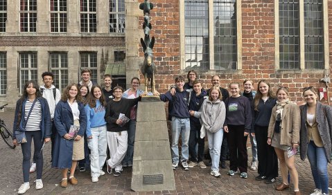 Eine große Gruppe junger Menschen steht um die Statue der Bremer Stadtmusikanten herum.