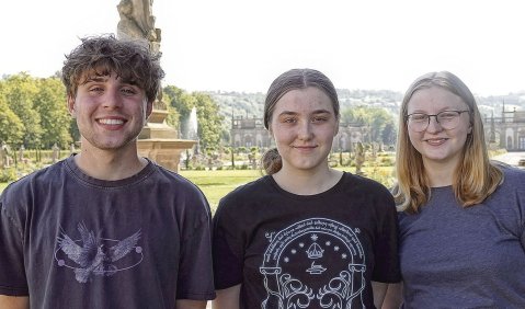 Drei junge Menschen in lockerer Kleidung mit einem prunkvollen Park im Hintergrund