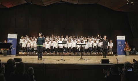 Eine Große Bühne mit einem sehr großen Kinderchor in schwarz-weißer Kleidung