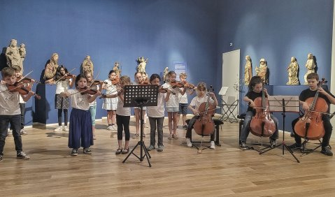 Holzboden, blaue Wand und ein Streichorchester mit kindlichen bis jugendlichen Teilnehmer*innen