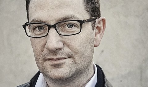 Gordon Kampe, in Jacke, hellem Hemd, mit dunklen kurzen Haaren, ohne Bart und mit schmaler Brille