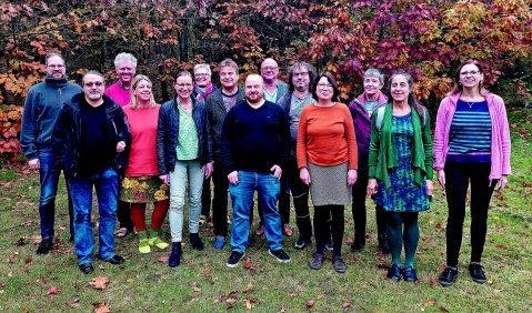 Die Menschen stehen in Alltagskleidung auf einer Wiese