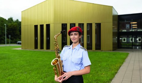 Eine Saxophonistin in Uniform vor dem modernen spitz-eckigen Bau des Musikzentrums der Waldkaserne Hilden.
