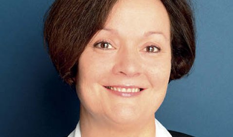 Eine Frau mit schwarzem Bob und freundlichem Lächeln vor blauer Wand.