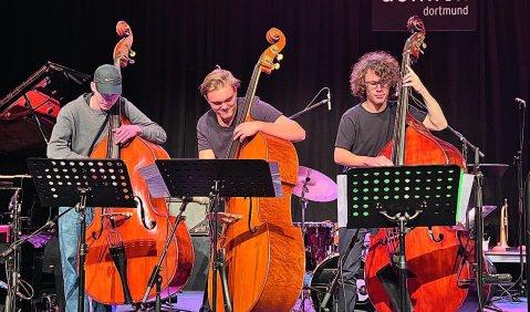 Drei Jazz-Kontrabässe auf einer bunt beleuchteten Bühne