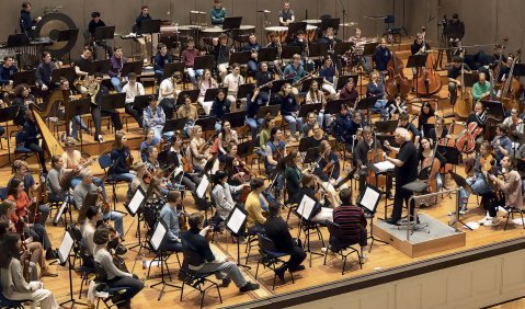 Das Jugendorchester in der Probe mit Rattle schräg von oben Fotografiert. Das junge orchester schaut gebannt zu Rattle.