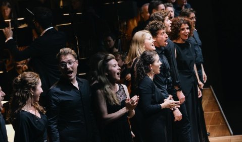 Vor dem Orchester an der Bühnenkante stehen die Sänger*innen gemischt