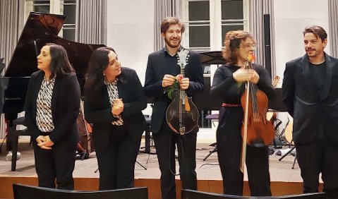 Ein Ensemble aus relativ jungen Erwachsen mit einer großen Bandbreite aus Instrumenten steht zum Applaus in einer Reihe.