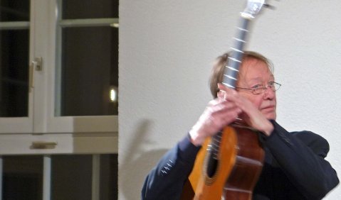 Ein älterer Gitarrist mit kurzen blonden Haaren in dynamischer Bewegung mit seiner Gitarre