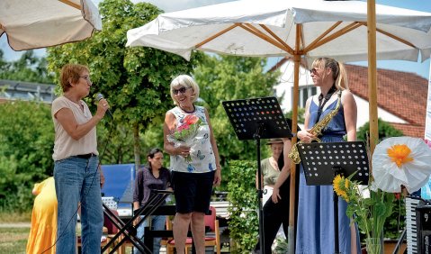Vier Frauen mittleren Alters auf einer kleinen Open-Air-Bühne unter weißen Sonnenschirmen.