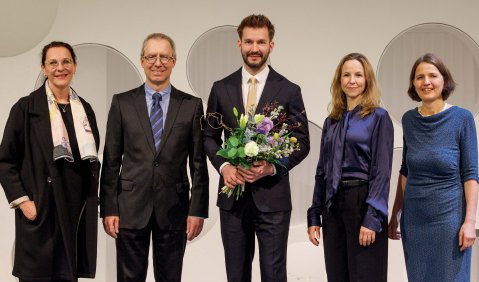 Fünf Personen in Anzügen, Robe und Kleidern. Lars Seniuk in der Mitte hält außerdem einen Blumenstrauß.
