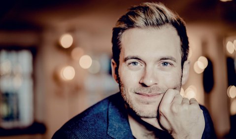 Ein Mann im niedrigen mittleren Alter mit kurzen blonden Haaren und blauem Sakko.