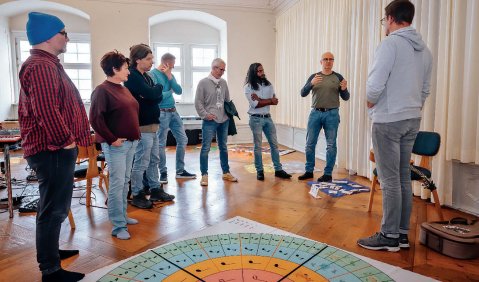 Ein geräumiger Seminarraum in einem Altbau: 8 Personen stehen in einem Halbkreis zusammen.