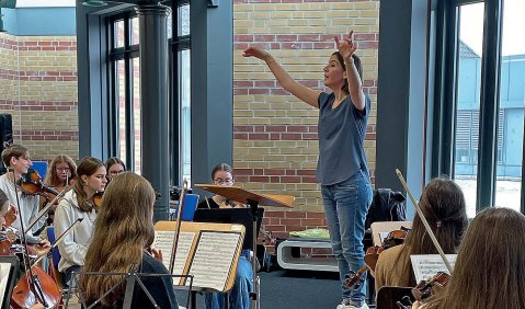 Eine Frau dirigiert ein Jugendorchester.