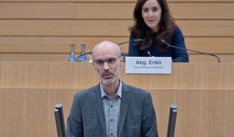 Ein Mann in mittlerem Alter mit glatze und Bart am hölzernen Redner:innen-Pult des Landtags Baden-Württemberg
