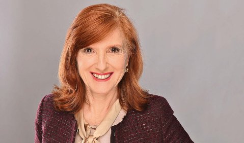 Porträt einer rothaariger Frau in höherem mittleren Alter in einem bordeaux-farbenen Blazer.