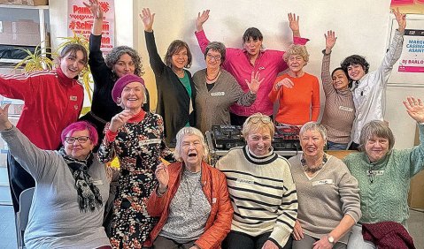 Zwei reihen Seniorinnen (und ein paar junge Menschen) winken in die Kamera.