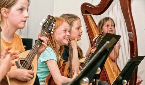 Ein Ensemble aus Kindern an verschiedensten Instrumenten (klar erkennen tut man Mandolinen und eine Harfe)