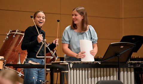Zwei (mit großem Spaß) hinter einem Xylophon stehende Mädchen in einem Orchesterprobensaal.