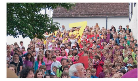 Ein Chor in Regenbogenfarben gekleidet singt einen Open-Air-Auftritt.