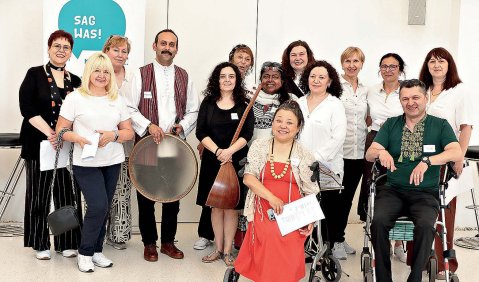 Mehrere Personen, teils auf Rollatoren sitzend, und an europäische Kulturen aber auch solche aus dem nahen Osten erinnernd stehen zu einem Gruppenfoto zusammen.