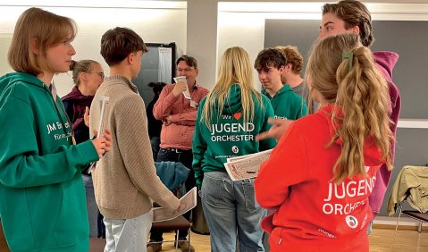 Mehrere jugendliche oder junge Erwachsene stehen in einem Raum beineinander.