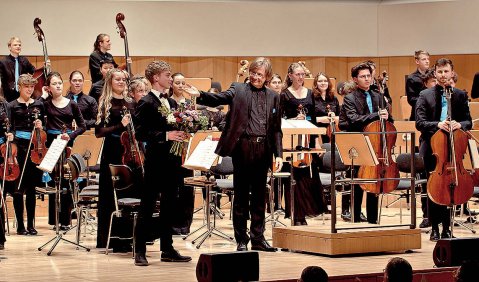 Foto von einem Orchesterkonzert beim Schlussapplaus. Bühne und Rückwand sind aus Holz.