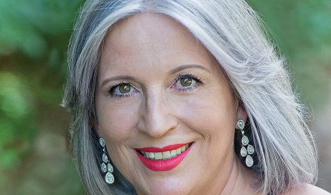 Eine Frau mit schwarzem Kleid, rotem Lippenstift, Ohrringen und silbernen Haaren.