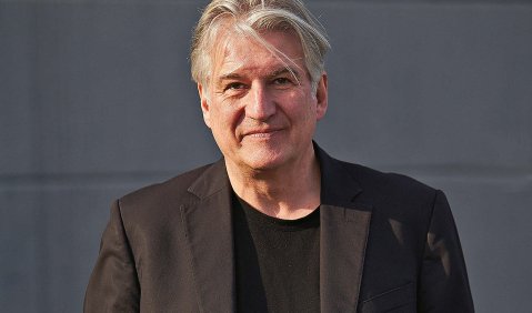 Ein Mann mit weißem Haar in schwarzem Anzug mit schwarzem T-Shirt.