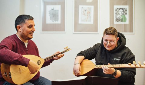 Zwei Menschen (ein Mann mittleren Alters und eine jüngere erwachsene Person) spielen Bağlama.