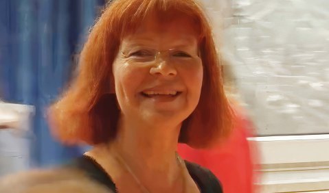Eine fröhlich lächlende Frau mit schulterlangen roten Haaren.