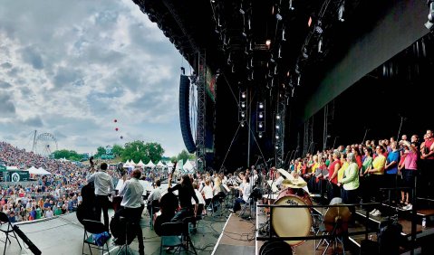Blick seitlich von einer Bühne auf eine riesige Publikumsmenge bei einem Open-Air-Konzert.