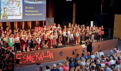 Ein großer Kinderchor auf einer Bühne. Oben hinter der Bühne wird etwas projiziert.