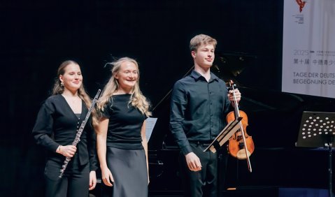Eine junge Querfl&ouml;tistin, eine Pianistin und ein Violinist stehen nebeneinander auf der B&uuml;hne und nehmen ihren Applaus entgegen.