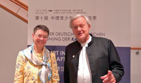 Ein &auml;lterer Mann in schwarzer Jacke und wei&szlig;em Hemd steht neben einer kurzhaarigen Frau in einem gelbgemusterten Oberteil.