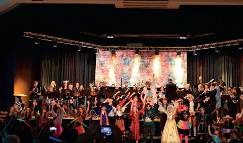 Ein gro&szlig;es Orchester und ein gro&szlig;er Chor bei einem gemeinsamen Auftritt in einer Art Stadthalle