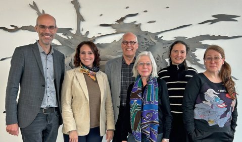 Die sechs Personen vor einem weißen Hintergrund mit einem großflächigen schwarzen Farbklecks.